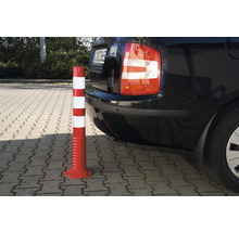 Rot-weißer Warnpfosten neben einem Auto auf einem Parkplatz.