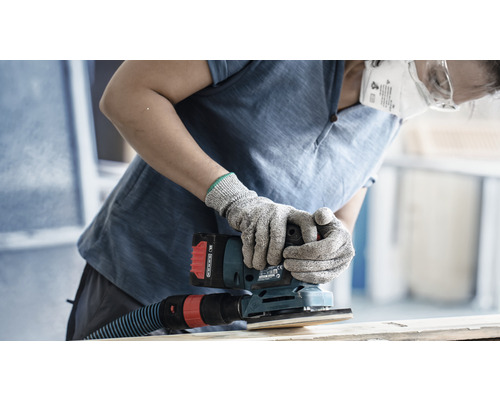 Eine Person schleift Holz mit einem Akku-Schwingschleifer, wobei sie Schutzhandschuhe und eine Staubmaske trägt.