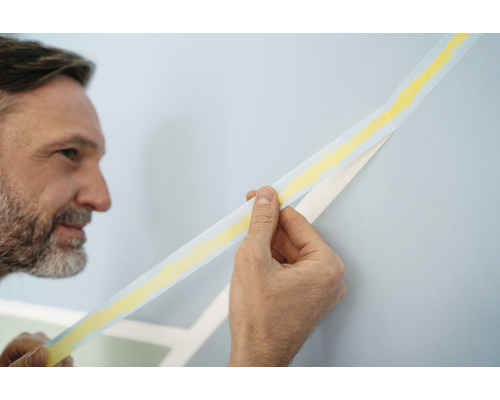 Mann entfernt Malerkrepp von Wand