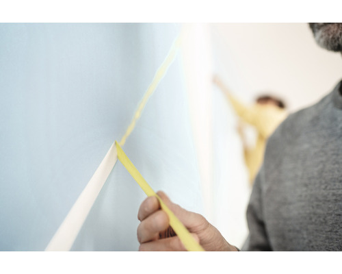 Ein Mann bringt Malerkrepp an eine Wand an.