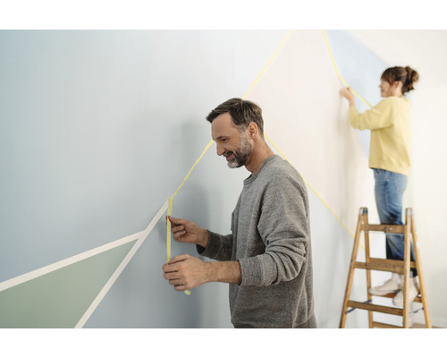Personen kleben Malerkrepp auf eine Wand für eine geometrische Gestaltung.