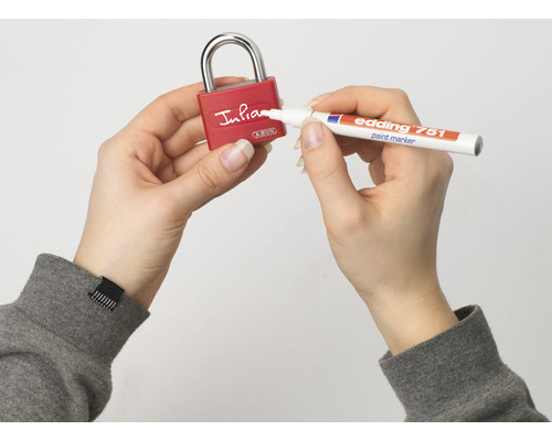 Eine Person beschriftet ein rotes ABUS Vorhängeschloss mit einem Edding 751 Lackmarker.
