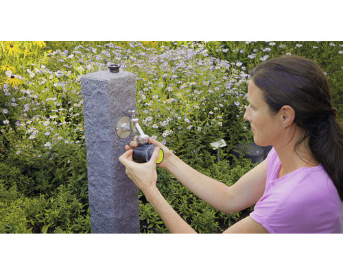 Frau schliesst einen Bewässerungscomputer an einen Wasserhahn im Garten an.