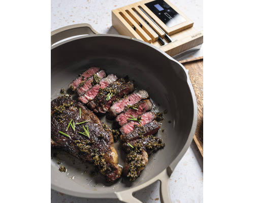 Gebratenes Steak in einer Pfanne mit einem Fleischthermometer im Hintergrund