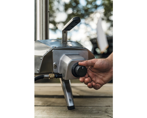 Ein Mann reguliert die Temperatur eines Pizzaofens im Freien mit einem Drehknopf.