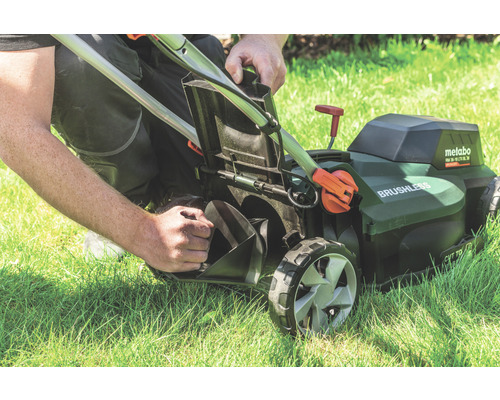 Ein Mann leert den Fangkorb eines Metabo Akku-Rasenmähers auf einer Rasenfläche.