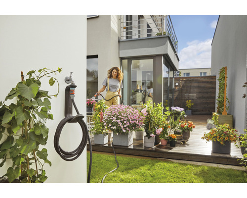 Frau gießt Blumen mit einem Gartenschlauch im Garten mit Schlauchhalterung