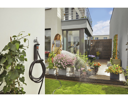 Frau bewässert Blumen mit einem Gartenschlauch auf einer Terrasse