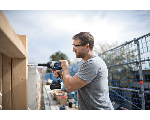 Handwerker mit Schutzbrille und Gehörschutz arbeitet mit einem Akku-Schlagschrauber an einem Holzrahmen