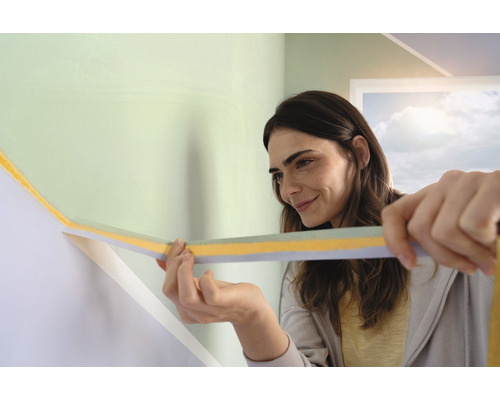 Frau bringt Abdeckband auf einer Wand an