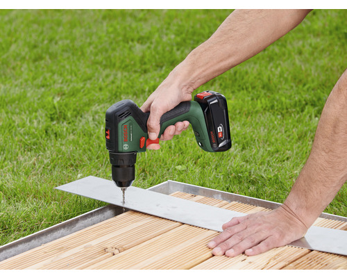 Akkuschrauber bohrt ein Loch in ein Metallstück auf einer Holzoberfläche.