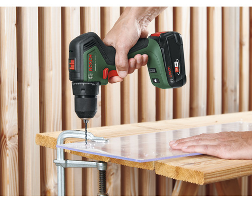 Eine Person bohrt mit einem Akku-Bohrschrauber von Bosch in eine Kunststoffplatte, die mit einer Schraubzwinge auf einer Holzoberfläche befestigt ist.