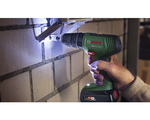 Eine Person bohrt mit einem Bosch Akku-Schlagbohrschrauber ein Loch in eine Ziegelwand.