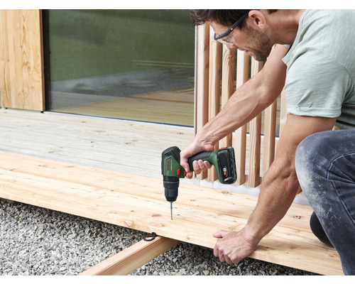 Ein Mann arbeitet mit einem Akkuschrauber an einer Holzterrasse.