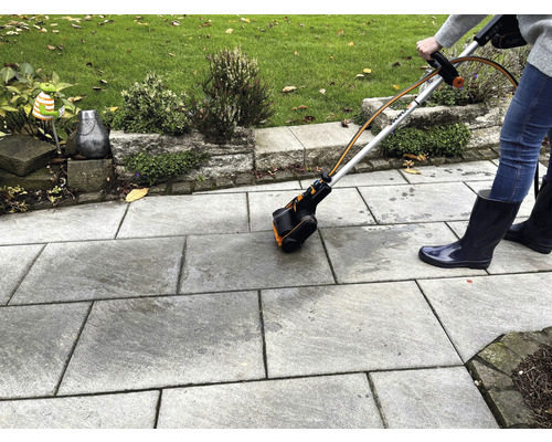 Person verwendet eine Fugenbürste zur Reinigung von Steinplatten im Freien.