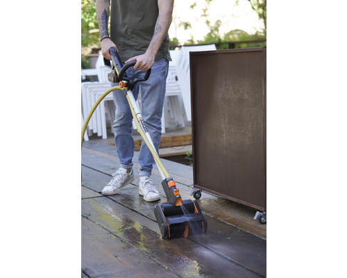 Eine Person reinigt eine Holzterrasse mit einem Terrassenreiniger von Worx.