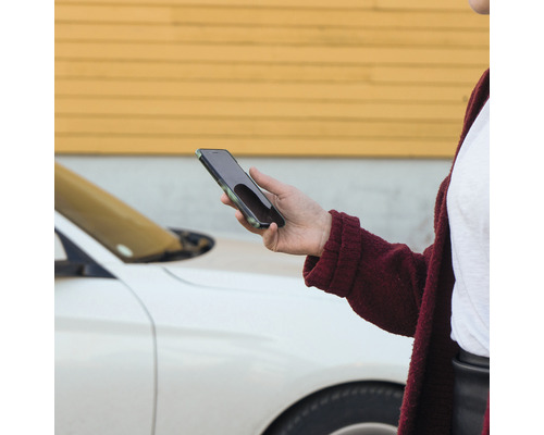 Eine Person hält ein Smartphone in der Hand, im Hintergrund ein Auto.