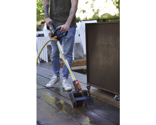 Eine Person benutzt einen Terrassenreiniger zum Reinigen einer Holzterrasse.