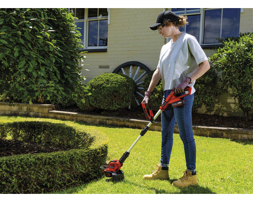 Frau benutzt einen Akku-Rasentrimmer im Garten.