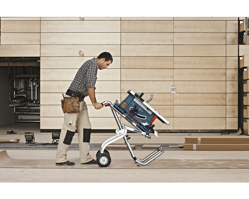 Mann transportiert eine Tischkreissäge mit einem Transportwagen auf einer Baustelle