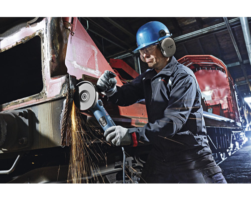 Mann mit Helm und Gehörschutz arbeitet mit einem Winkelschleifer an Metall, Funken fliegen.