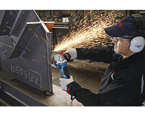 Ein Arbeiter benutzt einen Winkelschleifer an einem Metallstück, wobei Funken sprühen. Der Arbeiter trägt Schutzkleidung, inklusive Gehörschutz.