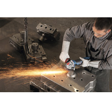 Mann schleift Metallteil mit einem Winkelschleifer in einer Werkstatt. Funken fliegen.