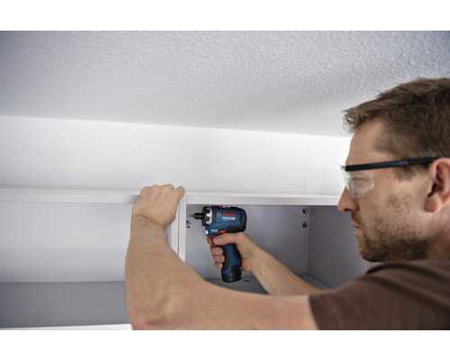 Mann befestigt Schrank mit einem Akkuschrauber der Marke Bosch