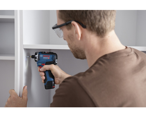 Mann schraubt Schraube mit Akku-Schlagschrauber in ein Regal