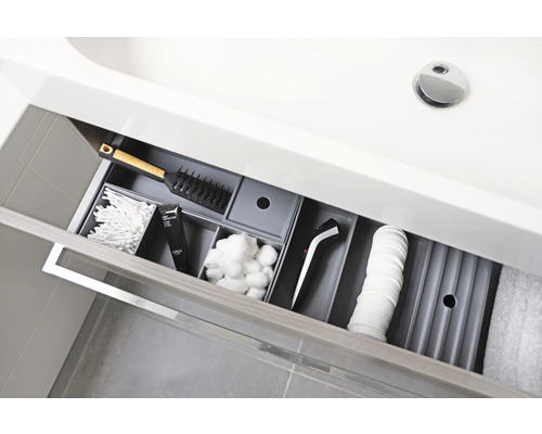 Geöffnete Schublade unter einem Waschbecken mit Kosmetikartikeln und einem Haarstylinggerät zur Aufbewahrung