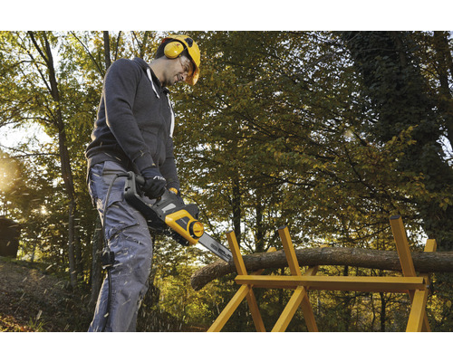 Mann sägt Holz mit einer elektrischen Kettensäge auf einem Holzbock im Freien.