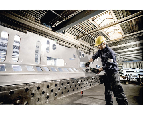 Metallarbeiter mit Schleifwerkzeug an Metallkonstruktion in Werkshalle