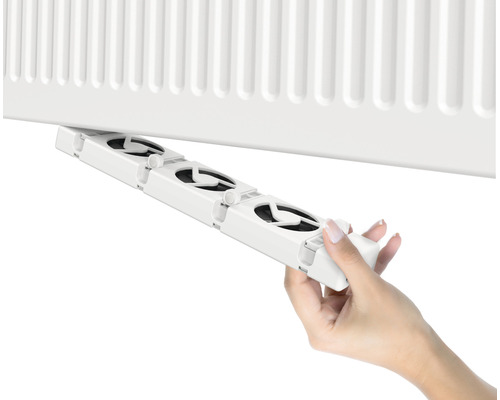 Eine Hand befestigt einen Heizkörperlüfter an einem Heizkörper.