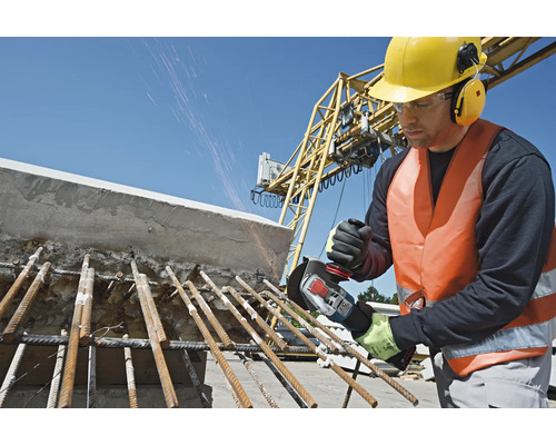 Ein Bauarbeiter mit Schutzhelm und Gehörschutz bearbeitet mit einem Winkelschleifer Stahlträger auf einer Baustelle
