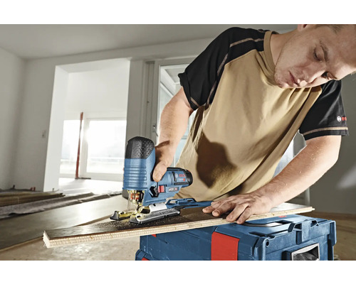 Ein Mann schneidet mit einer Stichsäge ein Brett auf einer Werkzeugkiste.