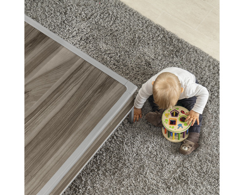 Kind spielt mit Formensortierspiel neben einem Tisch auf einem Teppich.