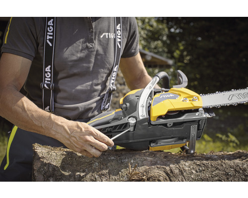 Eine gelbe und graue Kettensäge wird von einer Person mit einem Schraubenschlüssel auf einem Holzscheit justiert.