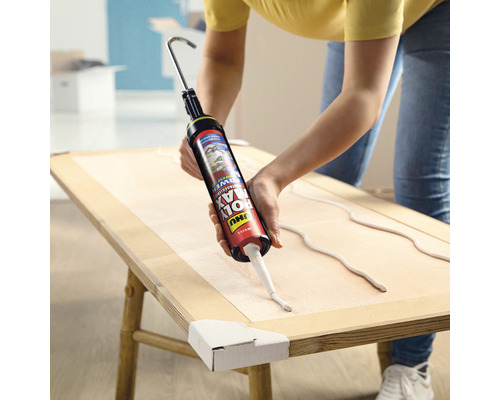 Eine Person trägt Klebstoff mit einer Kartuschenpistole auf ein Holzbrett auf.