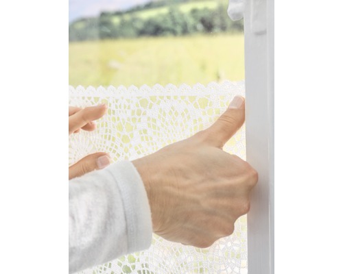 Person befestigt eine Fensterfolie mit Häkelspitze am Fenster