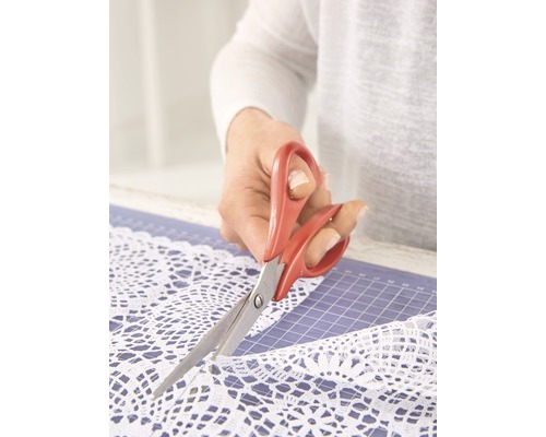 Eine Person schneidet weiße Spitze mit einer Schere auf einer Schneidematte.