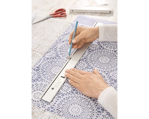 Person zeichnet mit Bleistift und Lineal auf Spitzentischdecke