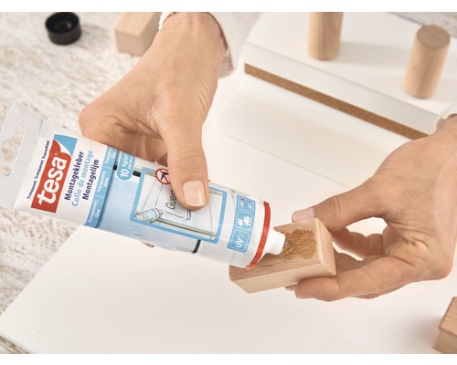 Eine Person trägt Montagekleber von Tesa auf ein Holzstück auf.