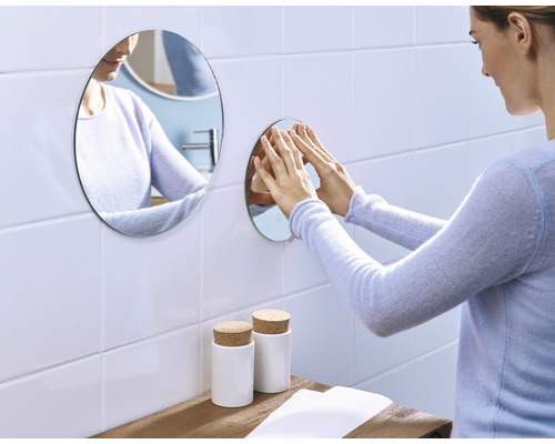 Frau befestigt runden Spiegel an Badezimmerwand