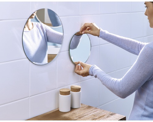 Frau befestigt runden Spiegel im Badezimmer an der Wand