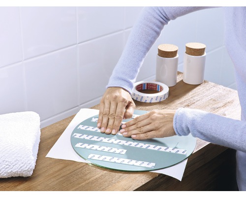 Eine Person befestigt Spiegelklebeband auf einem runden Spiegel auf einem Tisch.