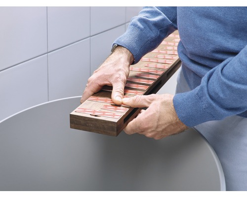 Mann hält Holzbrett mit Klebestreifen über einem Behälter