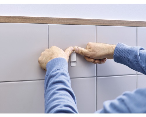 Person befestigt einen Haken an einer gefliesten Wand