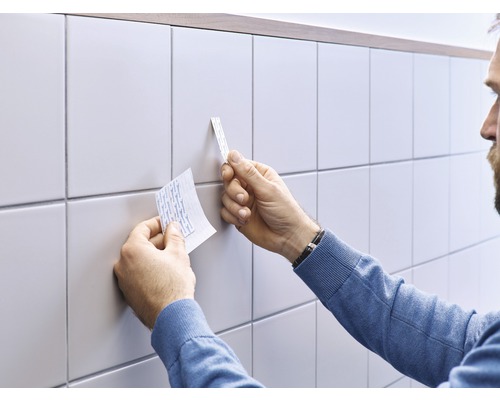 Eine Person befestigt doppelseitiges Klebeband an Fliesen