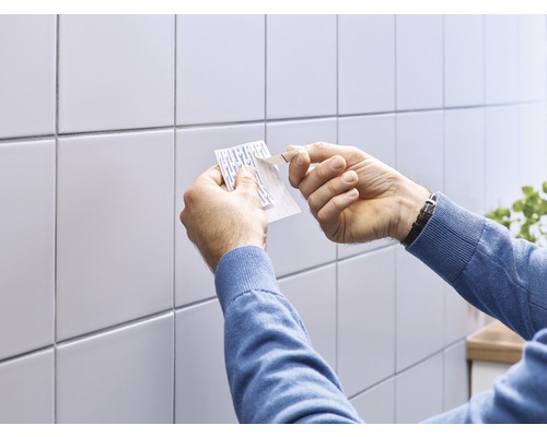 Mann befestigt einen Klebestreifen an einer Wand mit Fliesen