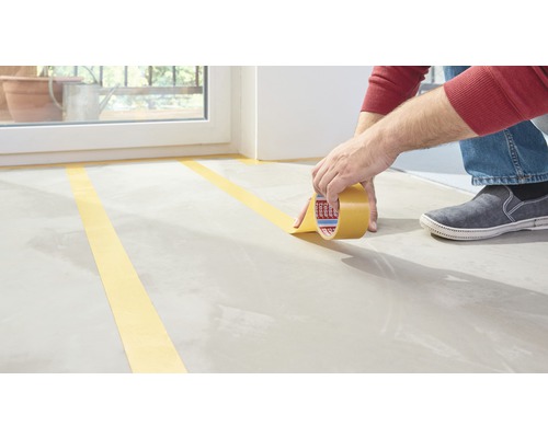 Person klebt Malerkrepp auf einen Boden.